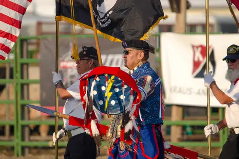 Three people holding flags and a shield in an outdoor setting.