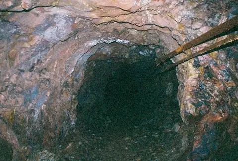 A view looking into a dark, rocky mine tunnel.