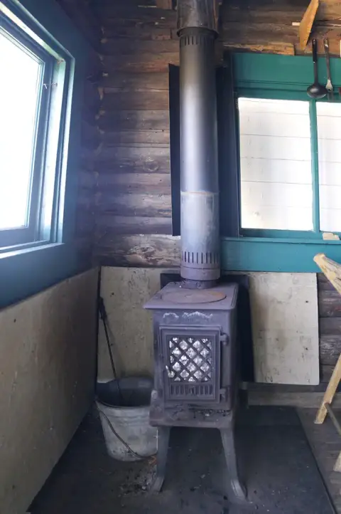 A wood stove sits inside a rustic cabin with log walls.