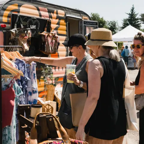 Three women browse clothing outside a colorful boutique trailer.