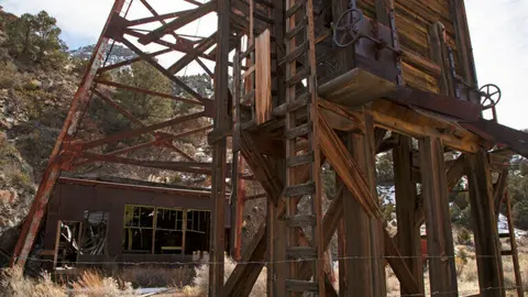 An old wooden mining structure stands outside against a hillside.