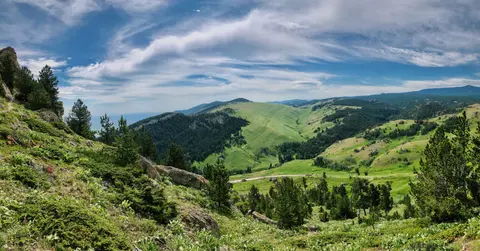 A wide panoramic view of a lush green mountainous landscape under a cloudy sky.