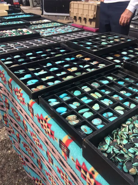 A vendor displays trays of turquoise stones at an outdoor market.
