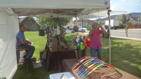 People running a craft booth at an outdoor market.