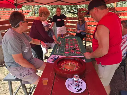 People gather around a roulette table outdoors under a canopy.