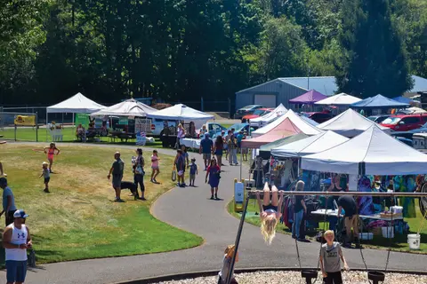 An outdoor market or fair with vendor tents, a walking path, and people on a sunny day.