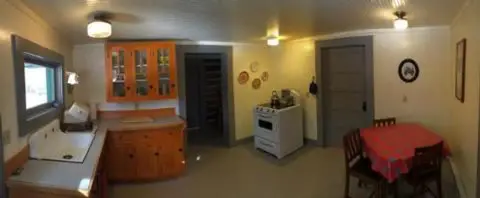 A wide-angle photo of a rustic kitchen interior with wooden cabinets and a dining table.