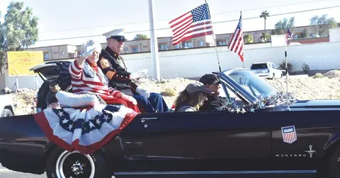 People waving from a convertible decorated with American flags in a parade.