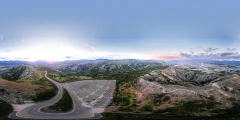 A 360 panoramic aerial view of a parking lot, winding roads, and mountainous landscape under a bright sky.
