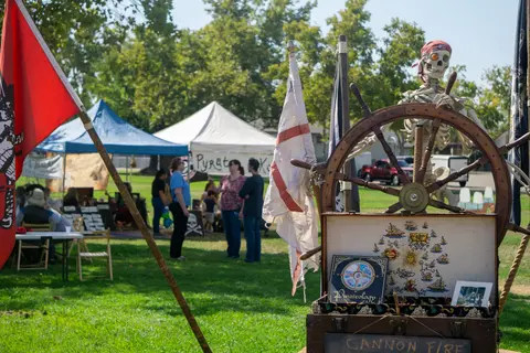 A pirate-themed display with a skeleton and ship's wheel is set up at an outdoor festival.