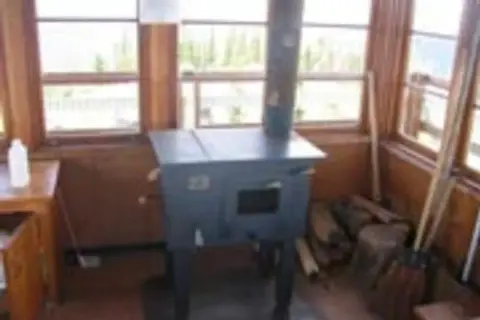 A wood stove sits inside a room with many windows.