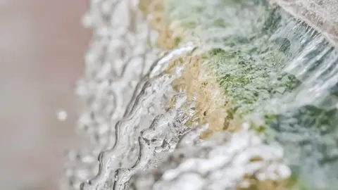 Water flows over a textured, colorful mineral ledge.