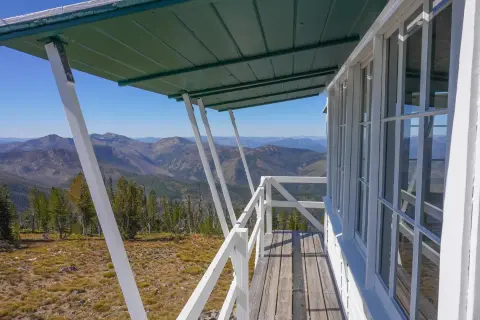 A view from the exterior balcony of a lookout tower overlooking mountains and forests.