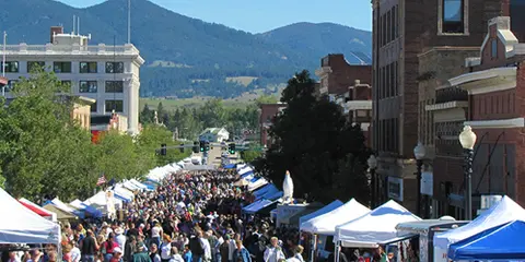 A crowded street market fills a city street lined with tents and buildings with mountains in the distance.