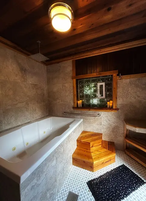 A bathroom interior with a large white bathtub, wooden steps, and tiled walls.