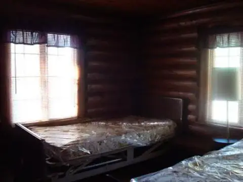 A bedroom inside a log cabin with two beds near windows.