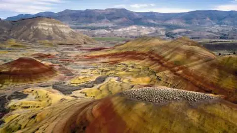 A high-angle landscape view of colorful banded hills and mountains under a partly cloudy sky.
