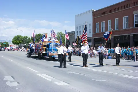 A parade with a decorated truck and flag bearers moving down a city street.