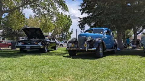 Classic cars are parked on a grassy area during an outdoor gathering.