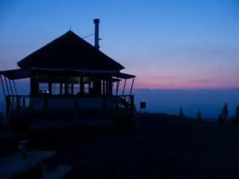 A fire lookout tower silhouette at dusk with a colorful sky in the background.