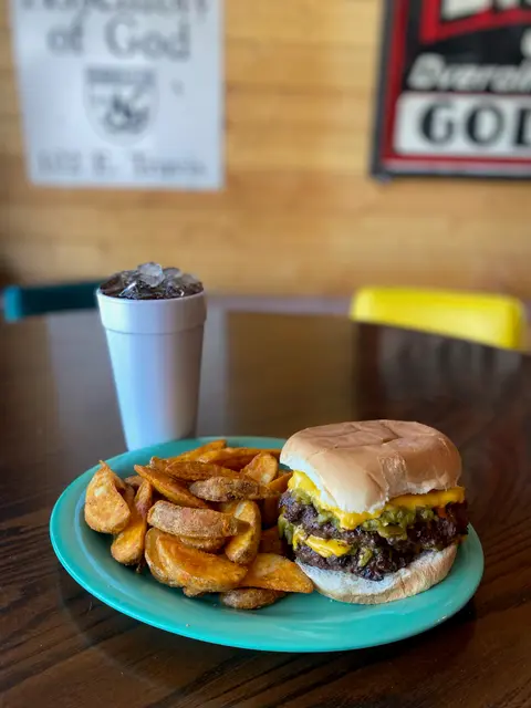 A double cheeseburger with potato wedges and a drink served on a green plate.