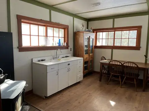 An interior view of a rustic kitchen with a sink, wooden cabinet, and dining table.