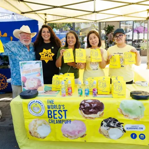 Five people pose behind a yellow vendor booth table displaying cream puffs.