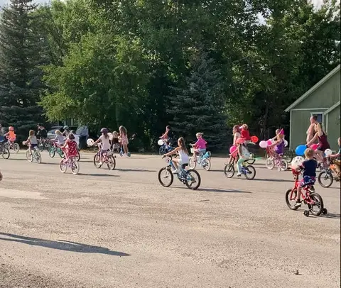Children ride bicycles decorated with balloons outdoors.