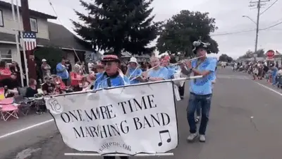 A marching band with a banner performing in a parade down a street.