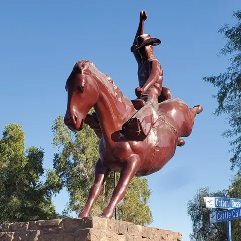 A brown statue of a cowboy riding a bucking horse against a blue sky.