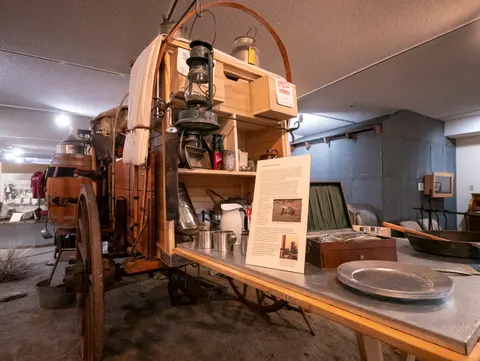 A historical chuck wagon and display table are set up inside a museum.