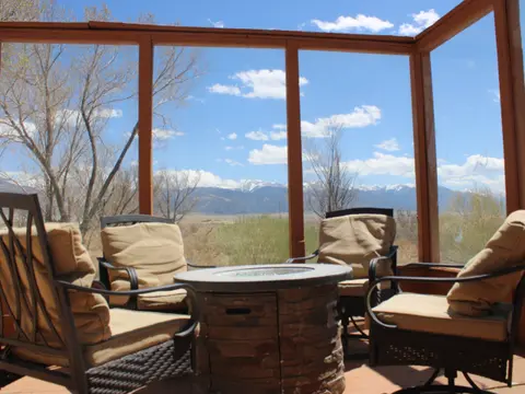 A view of mountains and a blue sky from inside a screen porch with chairs and a fire pit.
