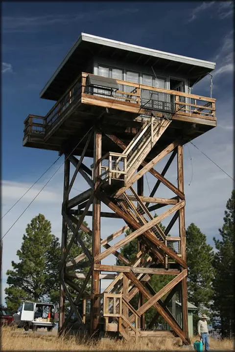 A tall wooden fire lookout tower stands outdoors under a blue sky.