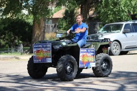 A young person sits on an ATV decorated with signs outdoors.
