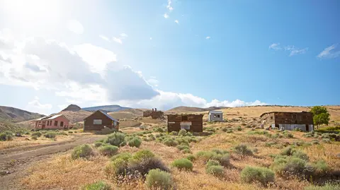 An old mining town with weathered wooden buildings set in an arid landscape under a bright blue sky.