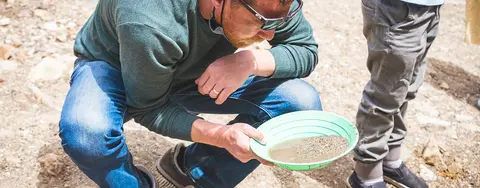 A man crouching down while panning for gold.