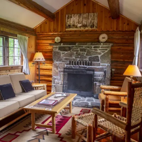 A cozy rustic living room featuring a stone fireplace and wooden furniture.