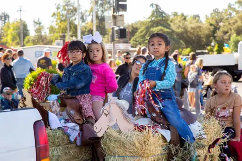 Children dressed up on a hay bale float holding red and white poms.