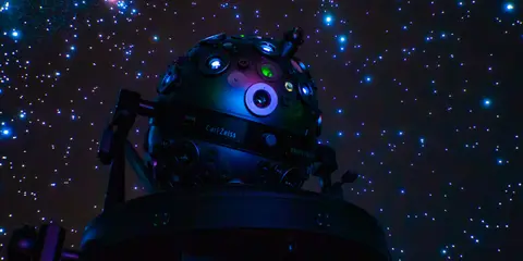 A planetarium projector is shown against a simulated starry night sky.