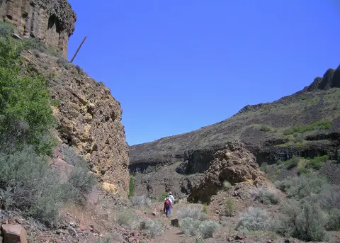 Hikers walk on a trail through a rocky canyon.