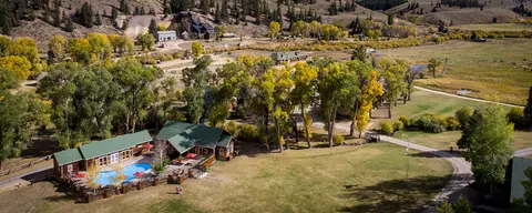 Aerial view of buildings, a pool, and trees in a valley with mountains in the background.