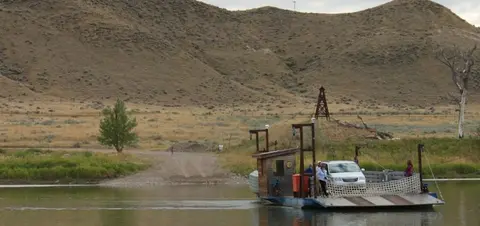A car and passengers on a ferry crossing a river.