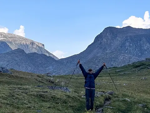 A hiker raises trekking poles in the air amidst a mountainous landscape.
