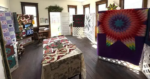 An interior view of a room displaying colorful quilts on stands and tables.
