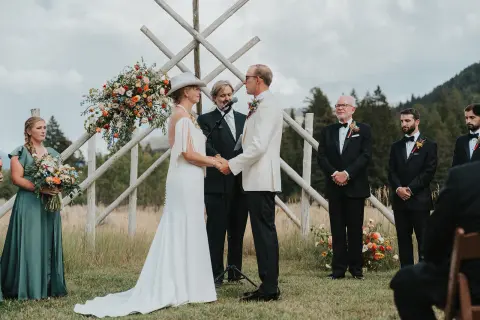 A bride and groom holding hands during an outdoor wedding ceremony.