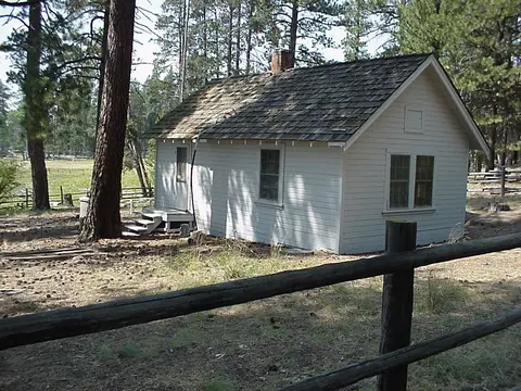 Exterior view of a small white wooden cabin in a forest clearing.