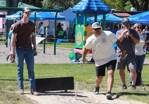 A man prepares to pitch a horseshoe at a park while others watch.