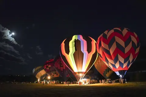 A night view of illuminated hot air balloons on a field under a moonlit sky.