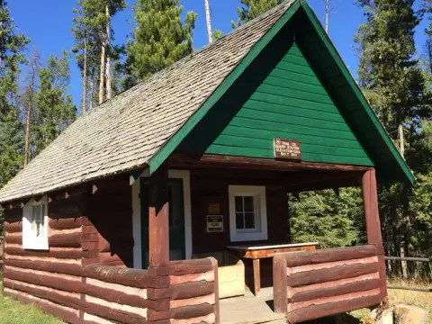 A wooden cabin with a porch stands surrounded by trees.