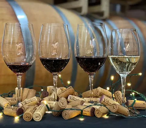 Four wine glasses filled with wine stand among wine corks and string lights.